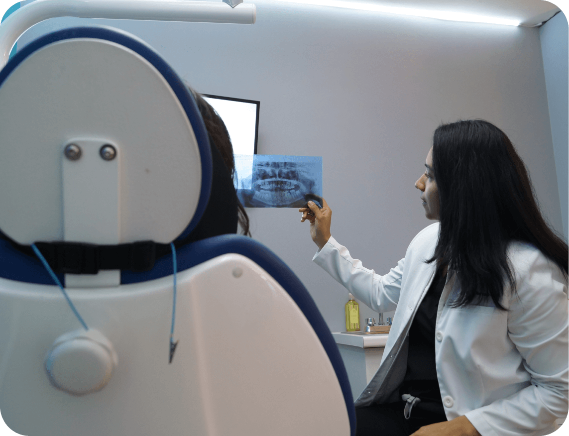 Dentista revisando una radiografía dental junto a una paciente sentada en una silla de dentista.