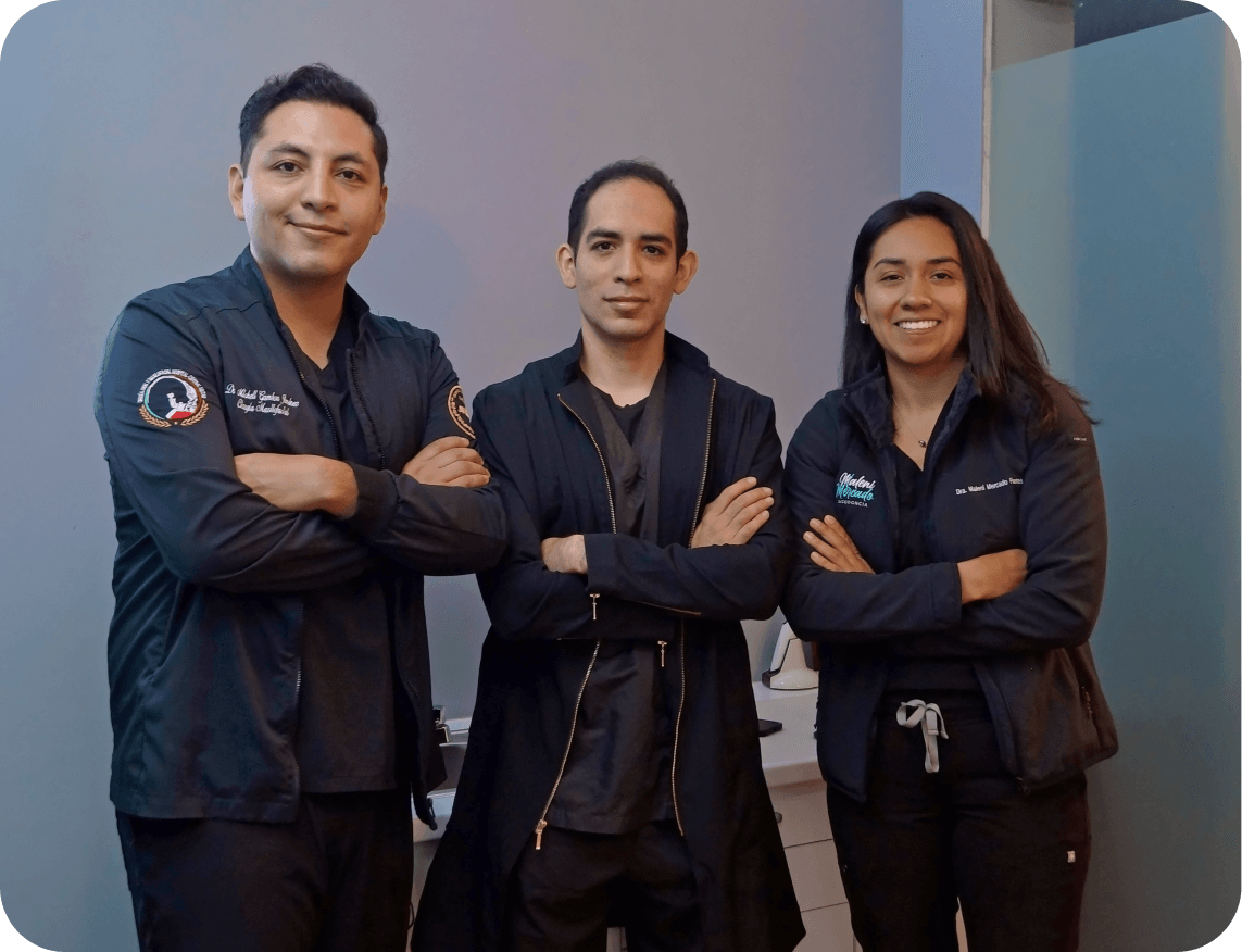 Tres profesionales de la salud con chaquetas negras, brazos cruzados, posando y sonriendo frente a una pared gris.