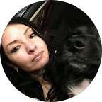 Mujer con cabello oscuro y expresión neutral abrazando a un perro negro de tamaño mediano.